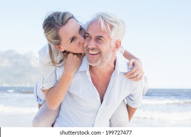 Man Giving His Smiling Wife A Piggy Back At The Beach On A Sunny Day