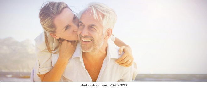 Man giving his smiling wife a piggy back at the beach on a sunny day