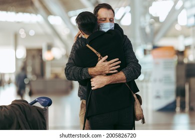 Man Giving Hug To Woman After Arrival From Trip Post Pandemic At Airport. Couple Meeting At Arrival After Long Separation During Pandemic At Airport.