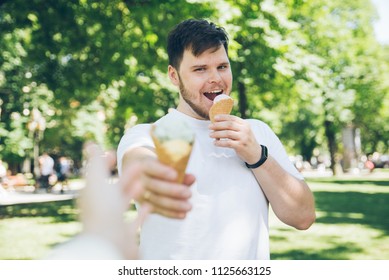 man giving ice cream in hot sunny day in city park. first person point of view reach out hand