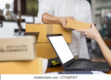 Man Giving Parcel Boxes To Woman With Open Laptop On Table