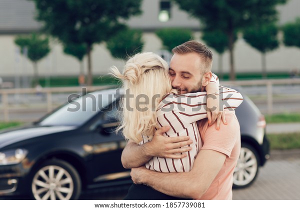 Man giving surprise to\
woman by purchasing a new car. Young couple buys a car, man and\
woman are hugging near the car on the street. Surprise gift for a\
loved one
