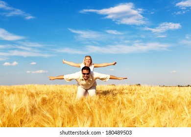 Man Giving A Woman Piggy Back In The Wheat Field