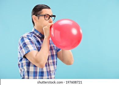 Man with glasses blowing up a balloon on blue background
