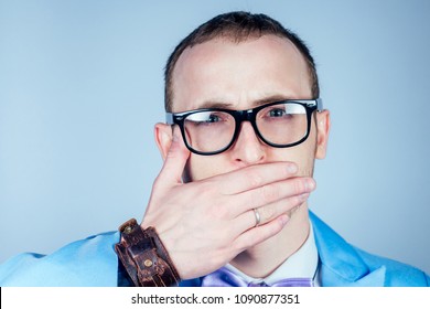 A Man With Glasses And A Blue Stylish Suit Covers His Mouth With His Hand. The Concept Of Secrecy, Confidentiality And Privacy