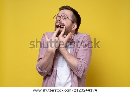 Man in glasses and casual clothes opened his mouth and shows a missing tooth with fingers. 