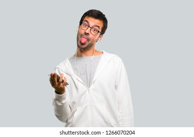 Man with glasses and listening music makes funny and crazy face emotion on grey background