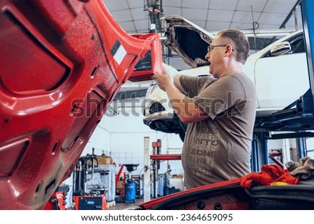 A Man with glasses Maintains a Auto in a Garage. Repair of Auto by an experienced Specialist in a Vehicle Repair Shop. Replacing the oil and filter. An autocar mechanic.