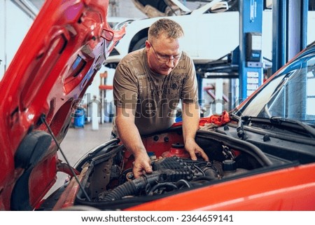 A Man with glasses Maintains a Auto in a Garage. Repair of Auto by an experienced Specialist in a Vehicle Repair Shop. Replacing the oil and filter. An autocar mechanic.