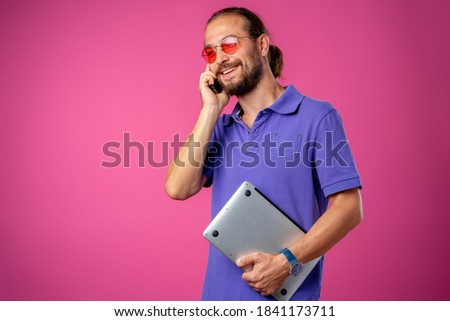 Man in glasses standing with laptop against pink background