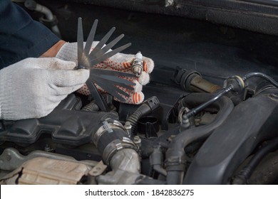 A Man With Gloves Checks The Spark Plug Gap With A Feeler Gauge