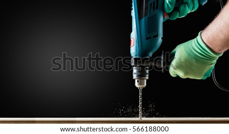 Man in Gloves Drilling wooden plank by Green Drill, close-up. Copy space.