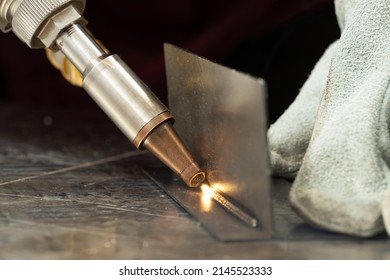 A man in gloves at the enterprise welds metal products by laser welding on a metal workbench. sparks fly