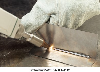 A man in gloves at the enterprise welds metal products by laser welding on a metal workbench. sparks fly