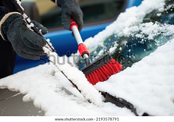 Man in gloves lifting windscreen wiper and brushing\
off snow