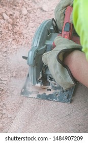 Man With Gloves On Using A Saw To Cut Concrete Creating Silica Dust From Cement Sidewalk