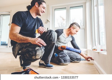 Man With The Glue Syringe Attaches Skirting To A Construction Site. Lay Parquet Floor