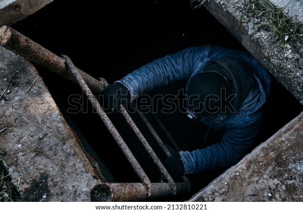 A man go down into the cellar along an iron\
ladder. People climbs a ladder from an underground bomb shelter.\
Hides and saves. Concept of wartime. No war. Underground life. Bomb\
shelter. Cold season.