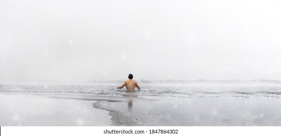 Man goes ice swimming into a frozen lake at snowfall