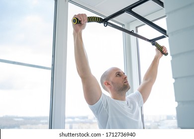 Man goes in for sports doing pull-up exercises on horizontal bar at his home - Shutterstock ID 1712736940