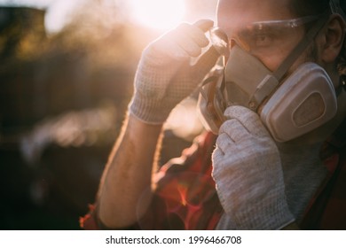 A man in goggles, gloves and a respirator. Means of protection. Young worker removes or puts on protective equipment during dusty and dirty work - Shutterstock ID 1996466708