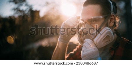 A man in goggles, gloves and a respirator. Means of protection. Young worker removes or puts on protective equipment during dusty and dirty work
