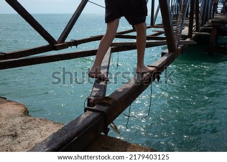 Man going and balancing on broken bridge over the river or sea. View on hole and blue water