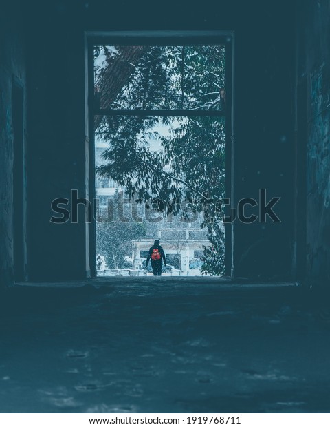 A man is\
going out of the building to face the winter and the snow wears an\
orange backpack and head to the\
forest