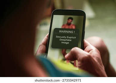 Man got warning message on his mobile phon for viewing AI generated sexualized imagery in social media using Deepfake technology. Selective focus on the phone.