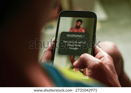 Man got warning message on his mobile phon for viewing AI generated sexualized imagery in social media using Deepfake technology. Selective focus on the phone.