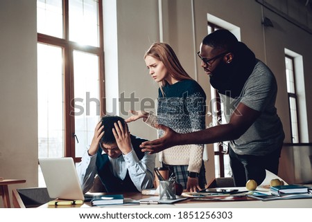 A man grabbed his head while colleagues scolded him for poor work. The worker at the table lowered his head and grabbed his head. 