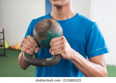 A man grasps firmly an old rusted kettlebell. Preparing to do a set of goblet squats. Working our at the gym.