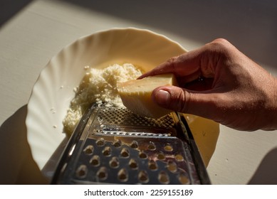 Man grating hard cheese. Ggrater and a plate with grated hard tasty cheese on a light background. Dairy. Concept: Italian cuisine, cheese, restaurant and food. Copy space - Powered by Shutterstock