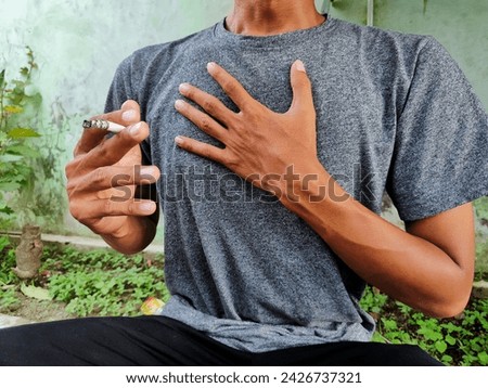A man in gray clothes whose right hand is holding a cigarette and his left hand is holding a tight chest.  Men who experience respiratory problems due to smoking.