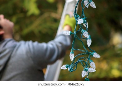 man in gray holding christmas lights climbs ladder