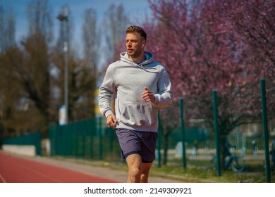 A man in a gray hoodie is jogging at a sports stadium. - Powered by Shutterstock