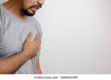 A man in a gray T-shirt holds his hand to his chest as sudden chest pain is an unhealthy sign leading to heart disease. Aortic stenosis and other ailments. White background. Empty space for text.