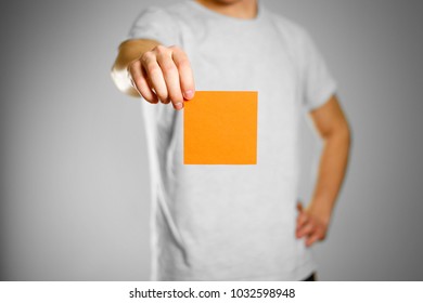 A man in a gray t-shirt holds a orange clean empty square sticker. Isolated on grey background.