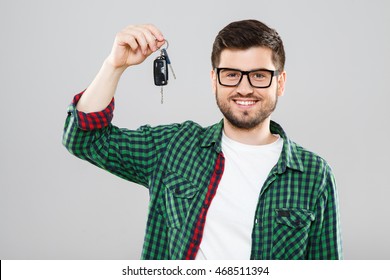 Man In Green Checked T-shirt And Eyeglasses Holding Car Keys. Looking At Camera, Smiling. Waist Up. Indoors, Studio