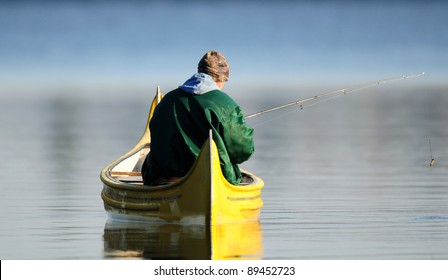 Man in green jacket fishing from bright yellow canoe - Powered by Shutterstock