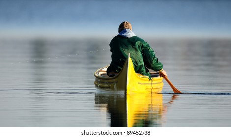 Man in green jacket paddling bright yellow canoe - Powered by Shutterstock