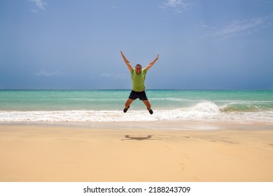 Man With Green Tshirt And Blue Shorts Jumping Alone On The Beach