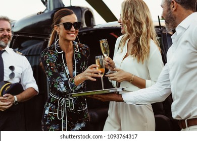 Man greet his female guests with wine. Women getting off a helicopter and picking up a welcome drink.