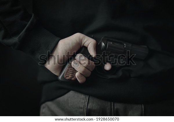 Man in grey cloth holds firearm behind his back.\
Revolver in men\'s hand. Criminal concept. Person ready to attack\
with hand gun.