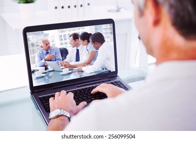 Man with grey hair typing on laptop against group of business people brainstorming together