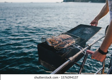 Man Grilling Fish On Yacht With Beautiful Ocean View.