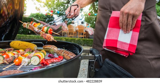 Man grilling meat on garden barbecue party, in the background friends eating and drinking - Powered by Shutterstock