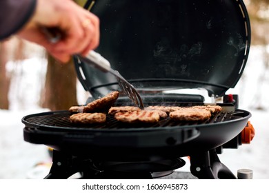 Man grilling steaks on a portable BBQ, Snowy winter barbecue outdoors in the cold . Outdoors winter barbecue party