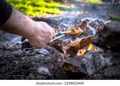 
A man grills meat kebabs on an open fire on a summer day. Male hand holding shish kebab close-up,