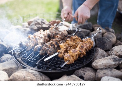 A man grills meat kebabs on an open fire on a spring day in the backyard of a private house.